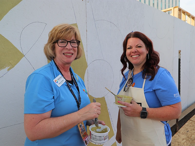 Two participants smiling together in front of the mural painting.