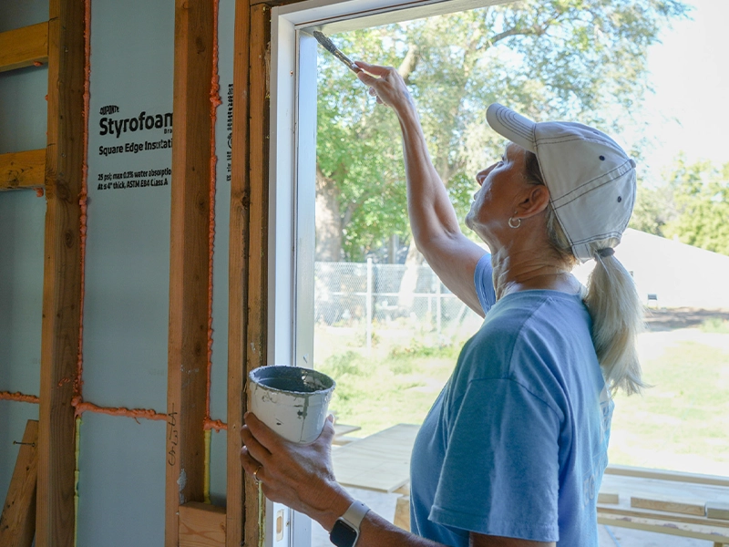 A volunteer painting the side of a window area.