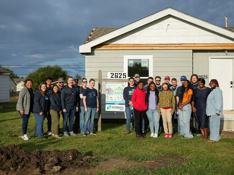A group of INTRUST Bank volunteers and Victoria's family standing in front of a house.