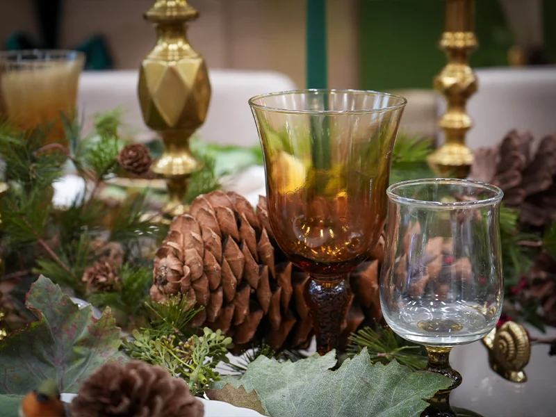 A vintage goblet on a table with pinecone and leaves.
