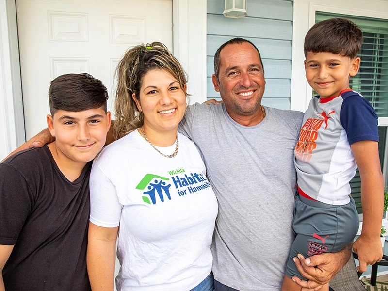A Habitat family smiling together in front of their home.